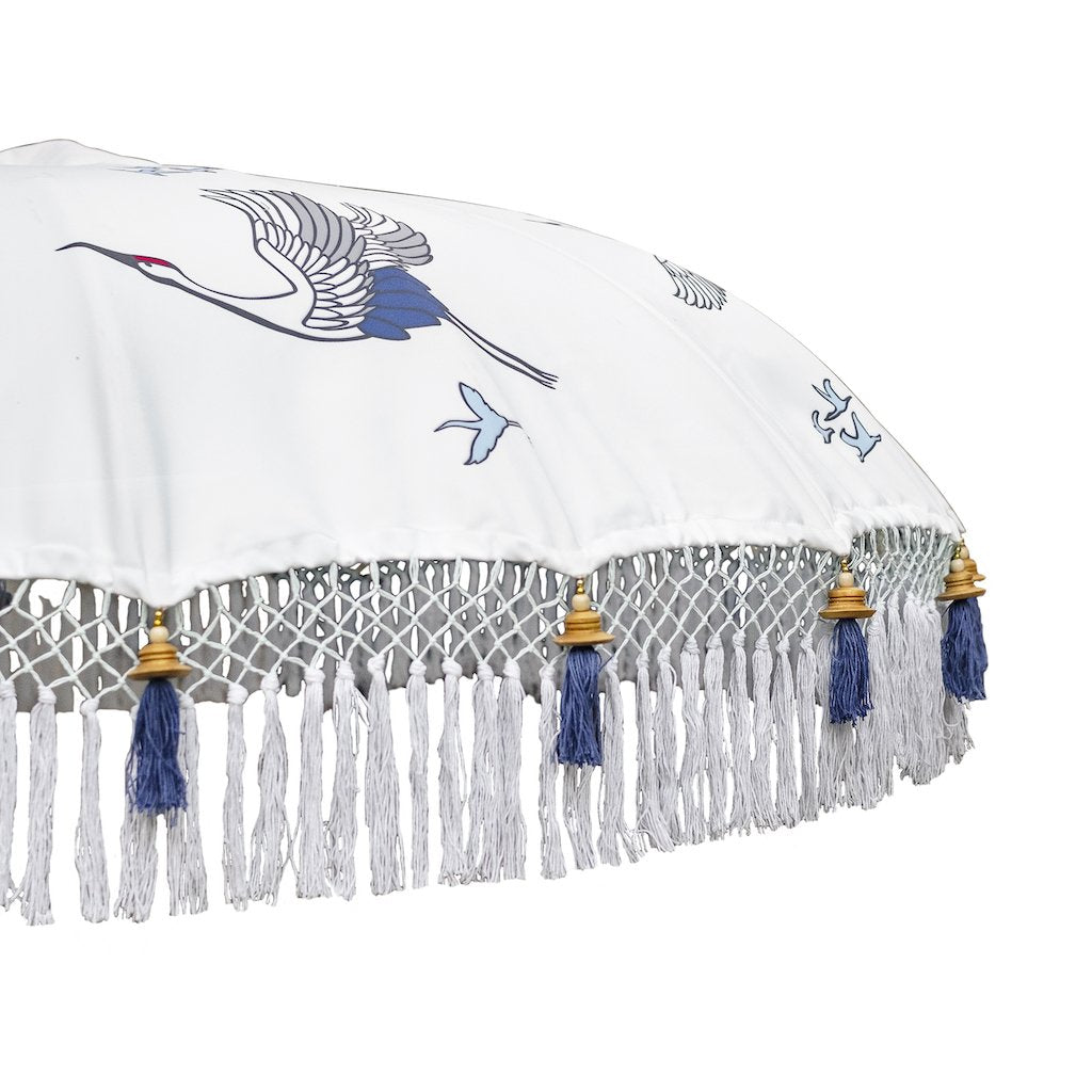 East London Parasol Lexi- flying birds and cranes printed on a bamboo garden parasol. White blue and indigo. Bali bamboo 2m garden umbrella with tassels in shades of white. A handmade piece and very special, a Japanese inspired parasol perfect to create a beautiful and elegant garden. A luxurious, maximalist garden decoration for a pool, patio, dining table and picnic.