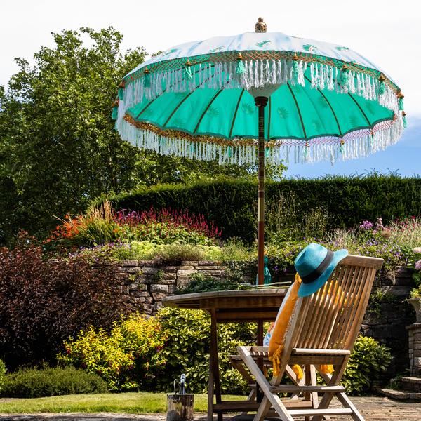 Catherine Parasol with turquoise cover and evil eye print in a lush garden