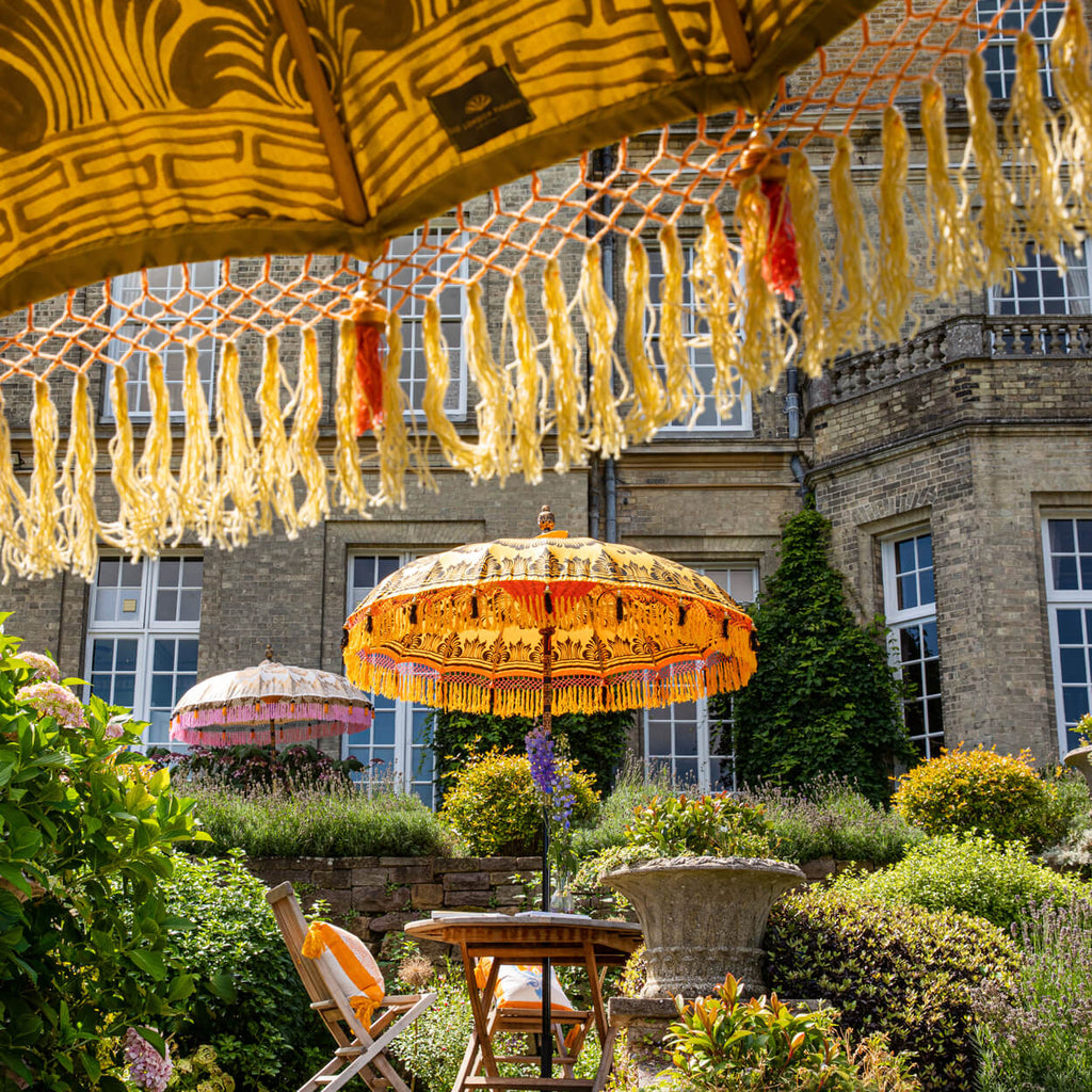 Helena Bamboo Parasol with hand painted gold lotus detail with pink and orange tassels in a garden