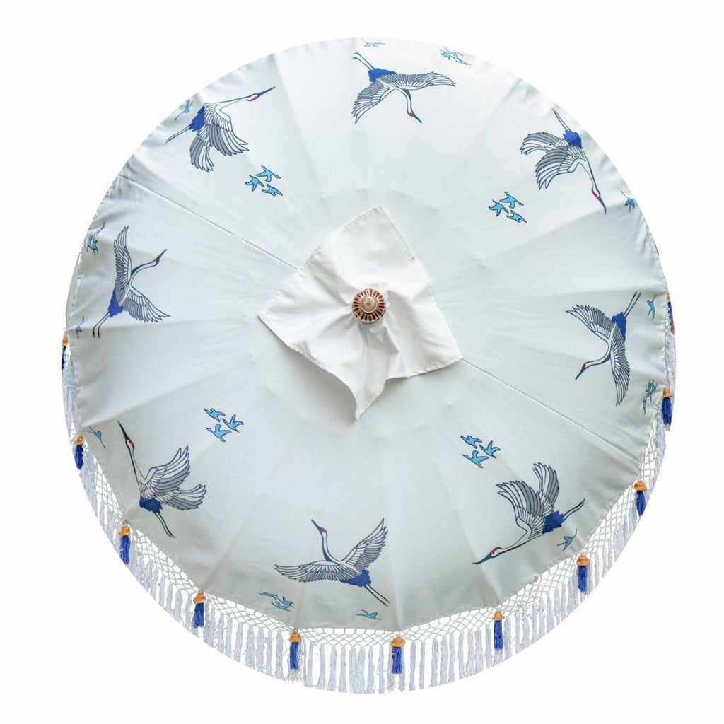 East London Parasol Lexi- flying birds and cranes printed on a bamboo garden parasol. White blue and indigo. Bali bamboo 2m garden umbrella with tassels in shades of white. A handmade piece and very special, a Japanese inspired parasol perfect to create a beautiful and elegant garden. A luxurious, maximalist garden decoration for a pool, patio, dining table and picnic.