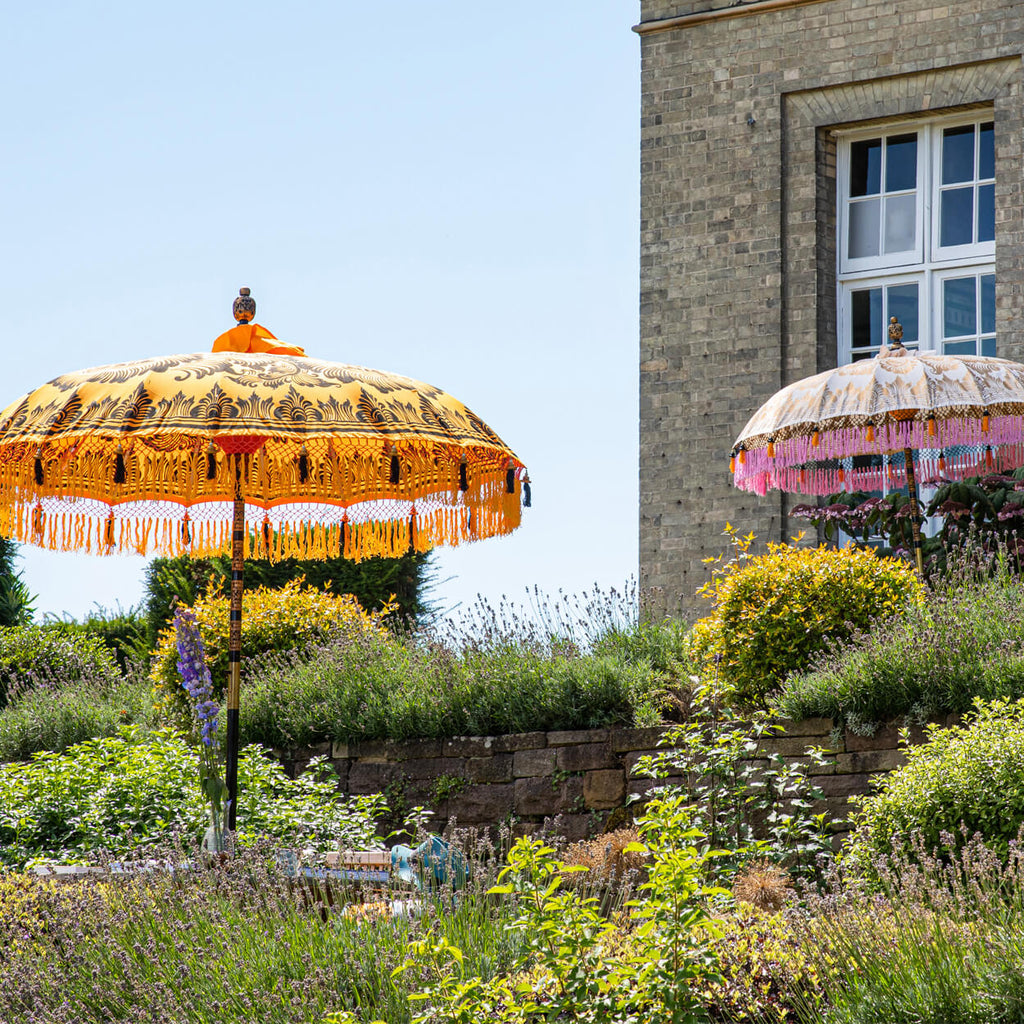 Helena Bamboo Parasol with hand painted gold lotus detail with pink and orange tassels in a garden